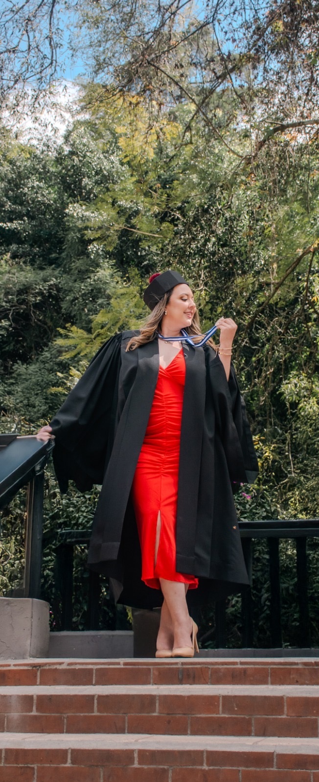 Graduada con toga negra y vestido rojo celebrando su logro